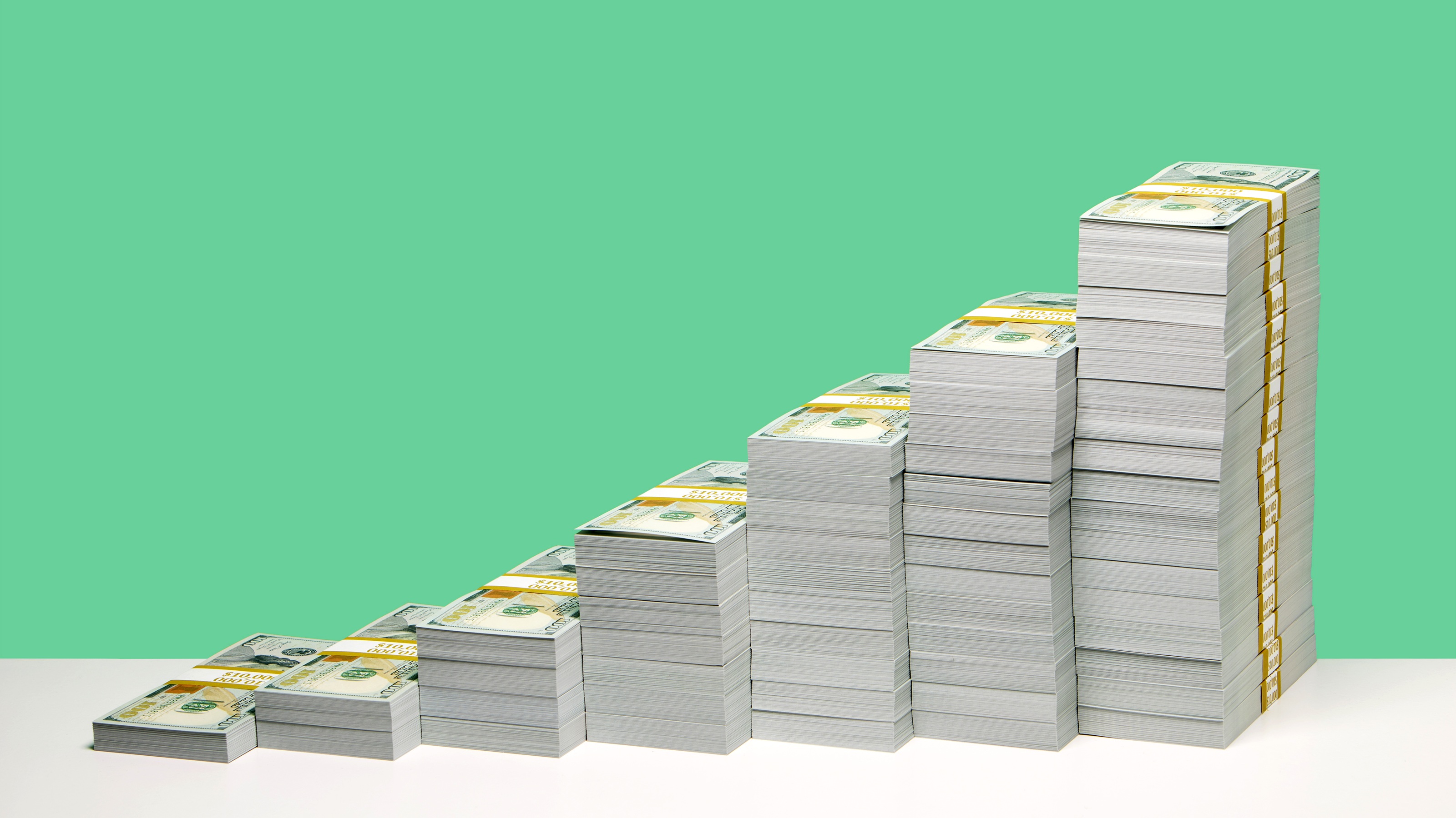 A series of cash stacks that grow progressively taller against a vibrant green background.