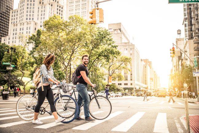 Two people walking bikes through a city crosswalk.