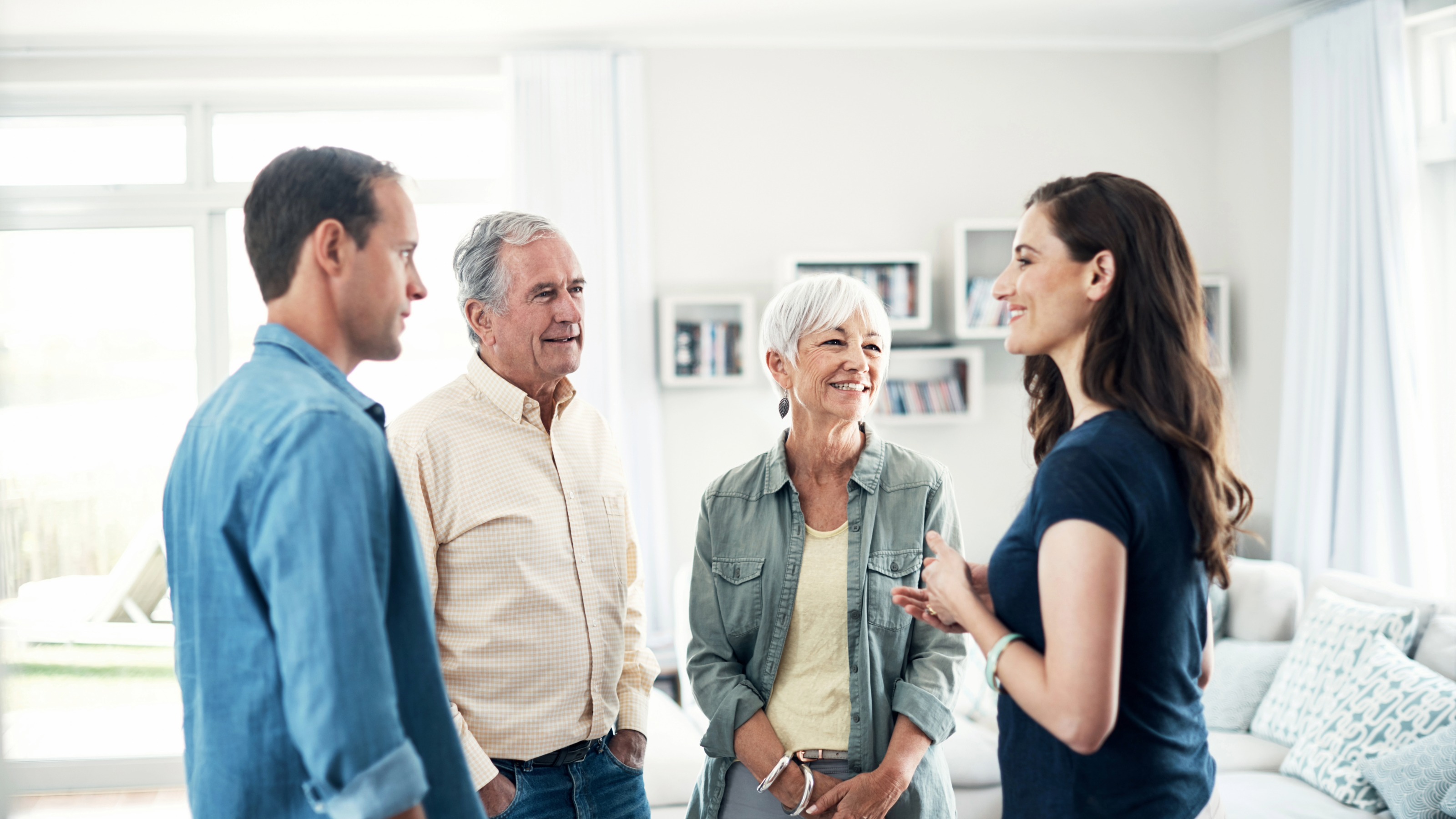 A multi-generational family group sitting together in a home living room engaged in conversation.