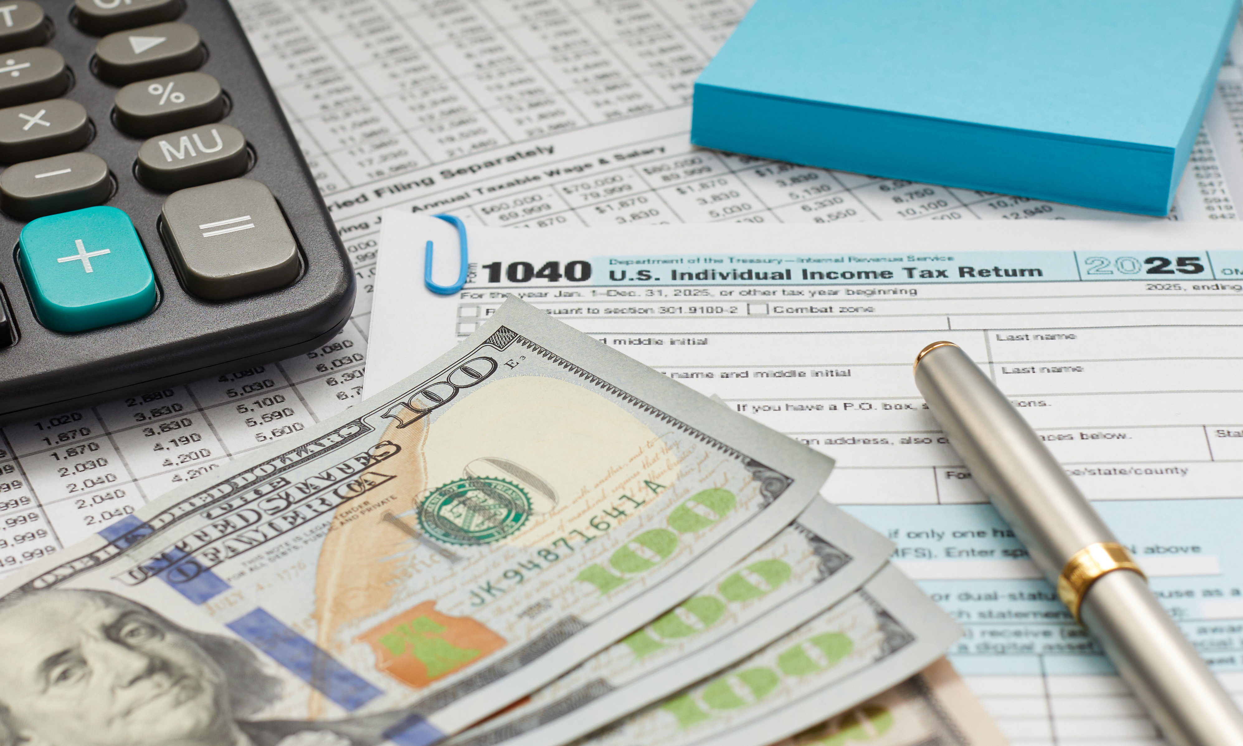 A desk with a calculator, pen, and tax forms prepared for a W-4 withholding adjustment.
