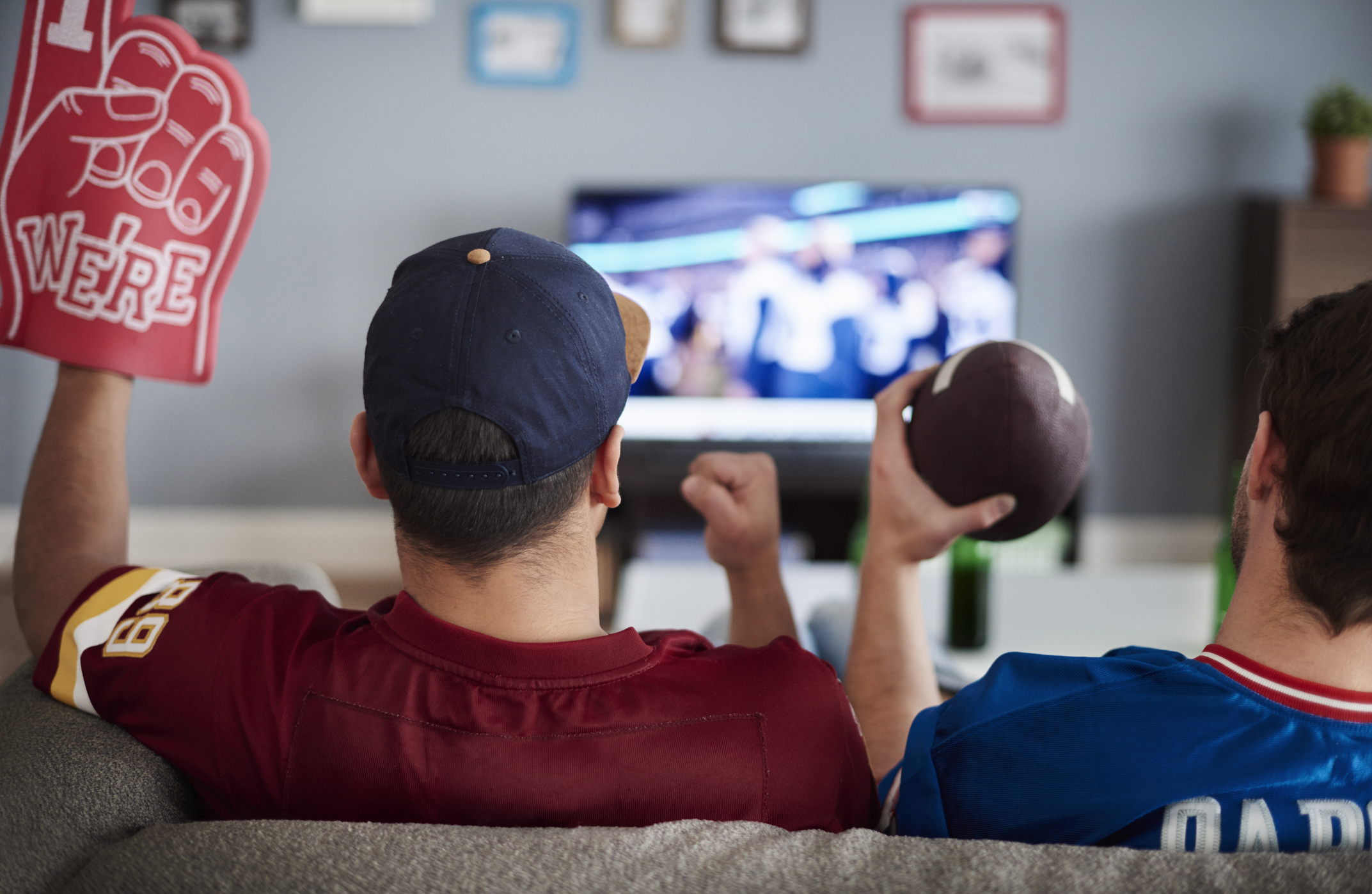 Two people sitting on a couch in a living room while streaming a football game on a television.