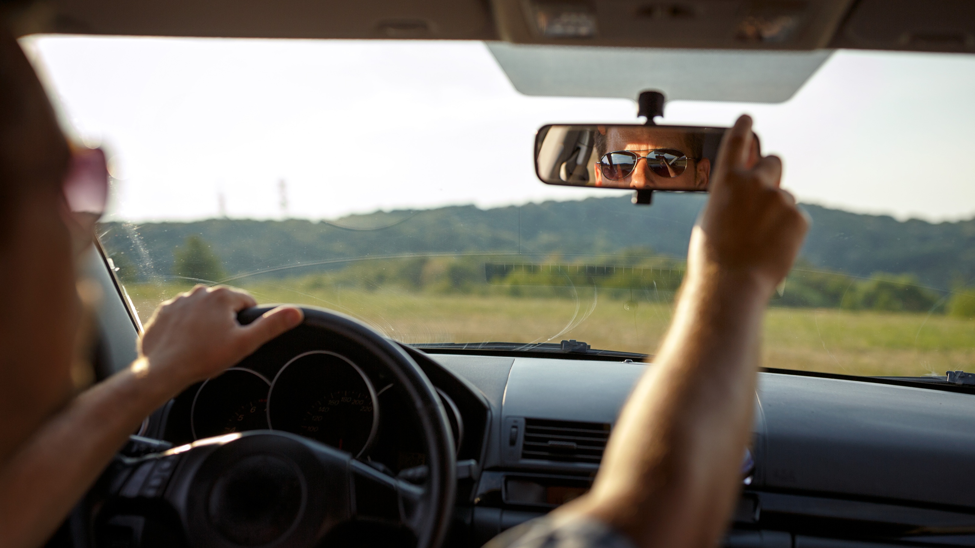 A person adjusting a car's rearview mirror while driving during the day.