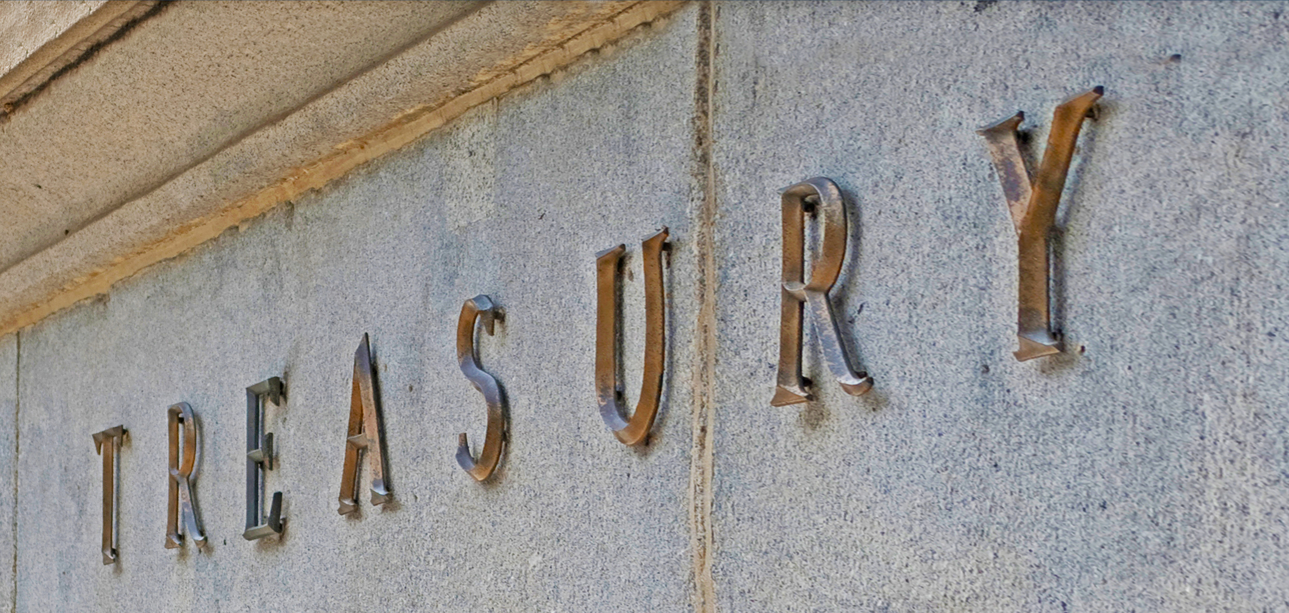 Brass letters spelling the word treasury mounted on a marble wall.