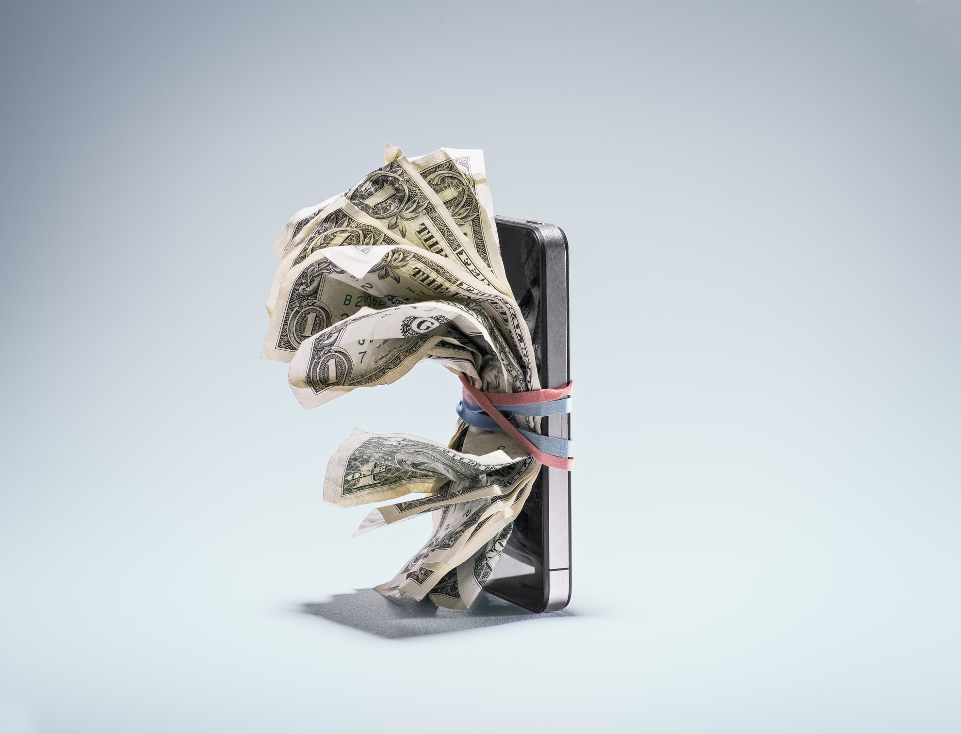 A smartphone with several banknotes secured to it by thick rubber bands.