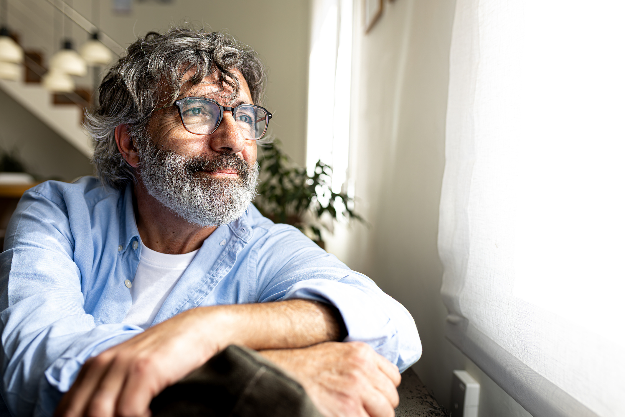 A man looking calmly out of a window in a bright room, representing mental clarity and reduced financial worry.