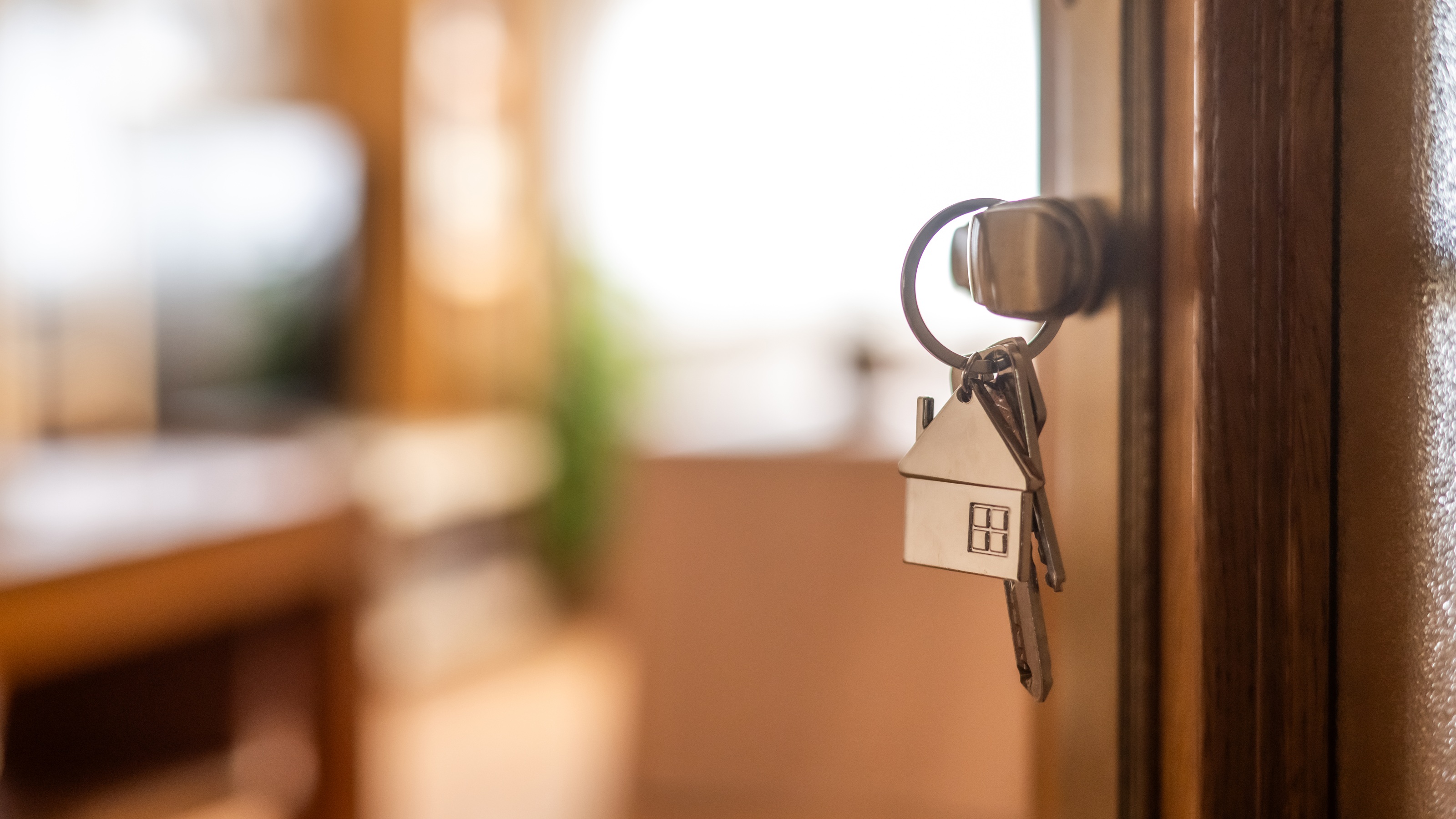 A close-up of house keys with a home-shaped keychain hanging from a door.