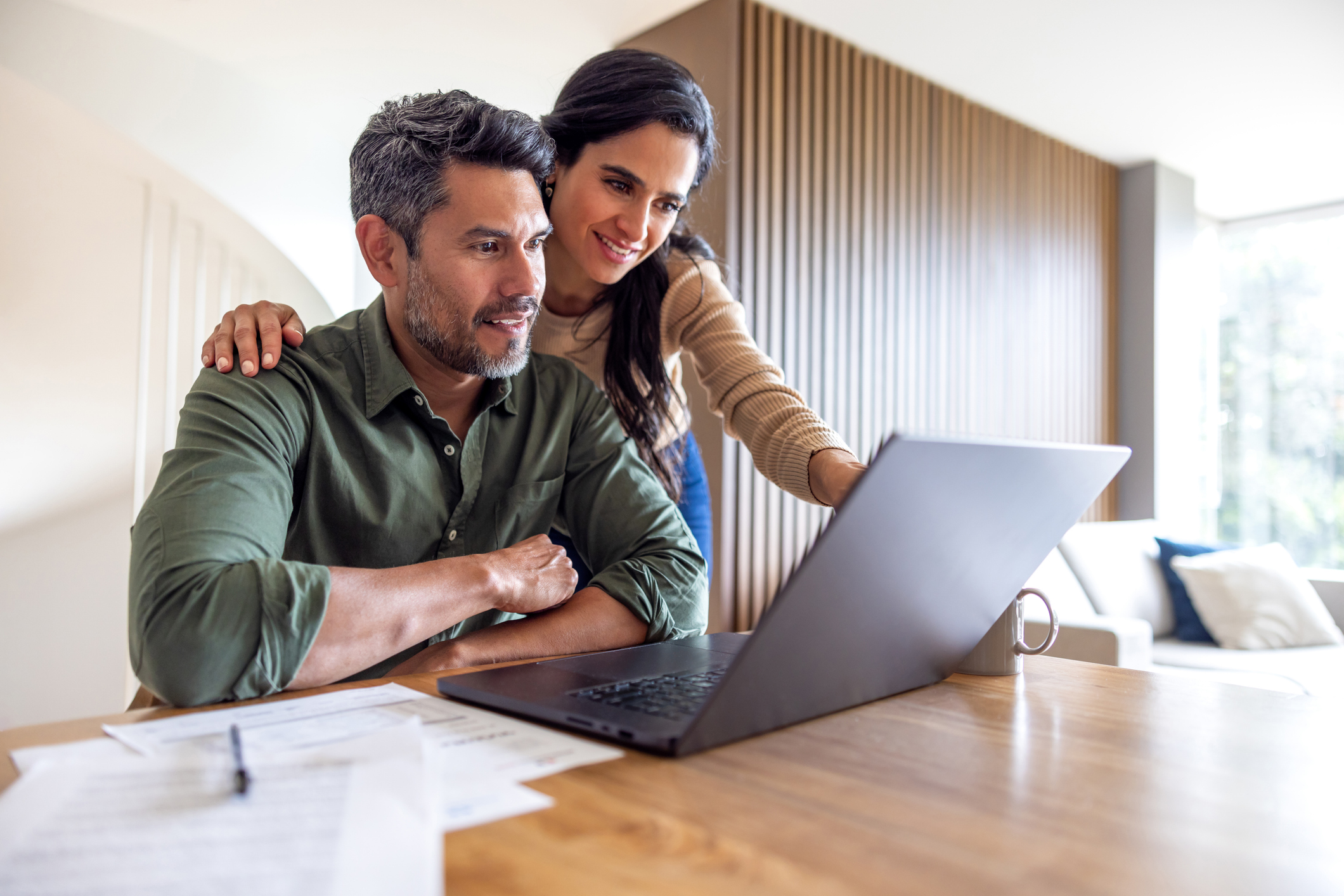 A couple smiling while reviewing their successful financial progress and savings on a mobile device.