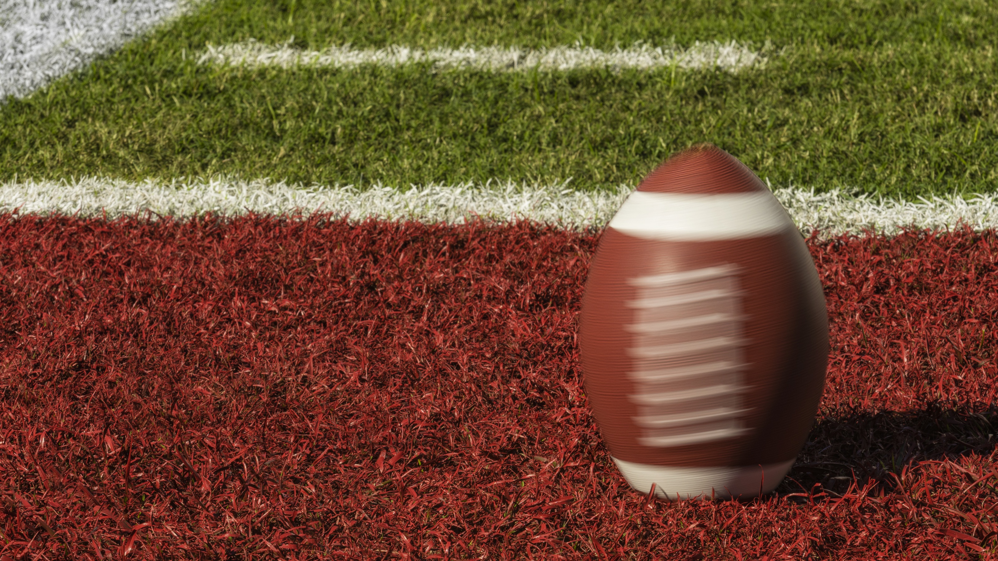 A close-up of a football spinning on the grass in the red zone of an empty stadium field.