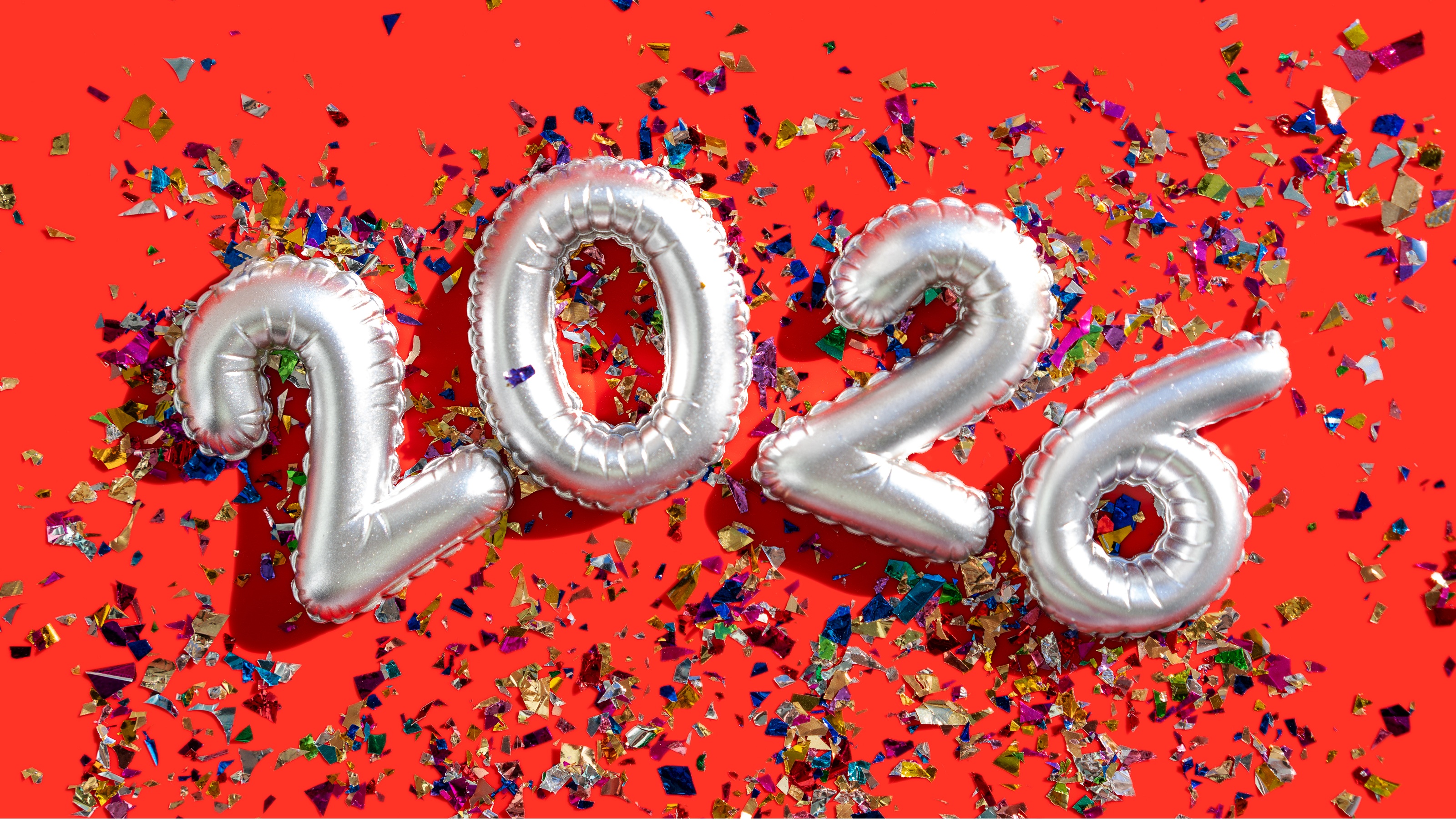 Silver balloons spelling out 2026 against a festive red background with confetti.