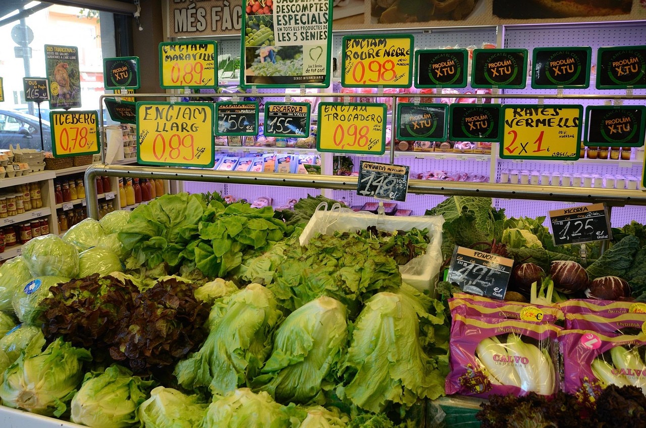 Fresh carrots and green vegetables in a market display with price tags.