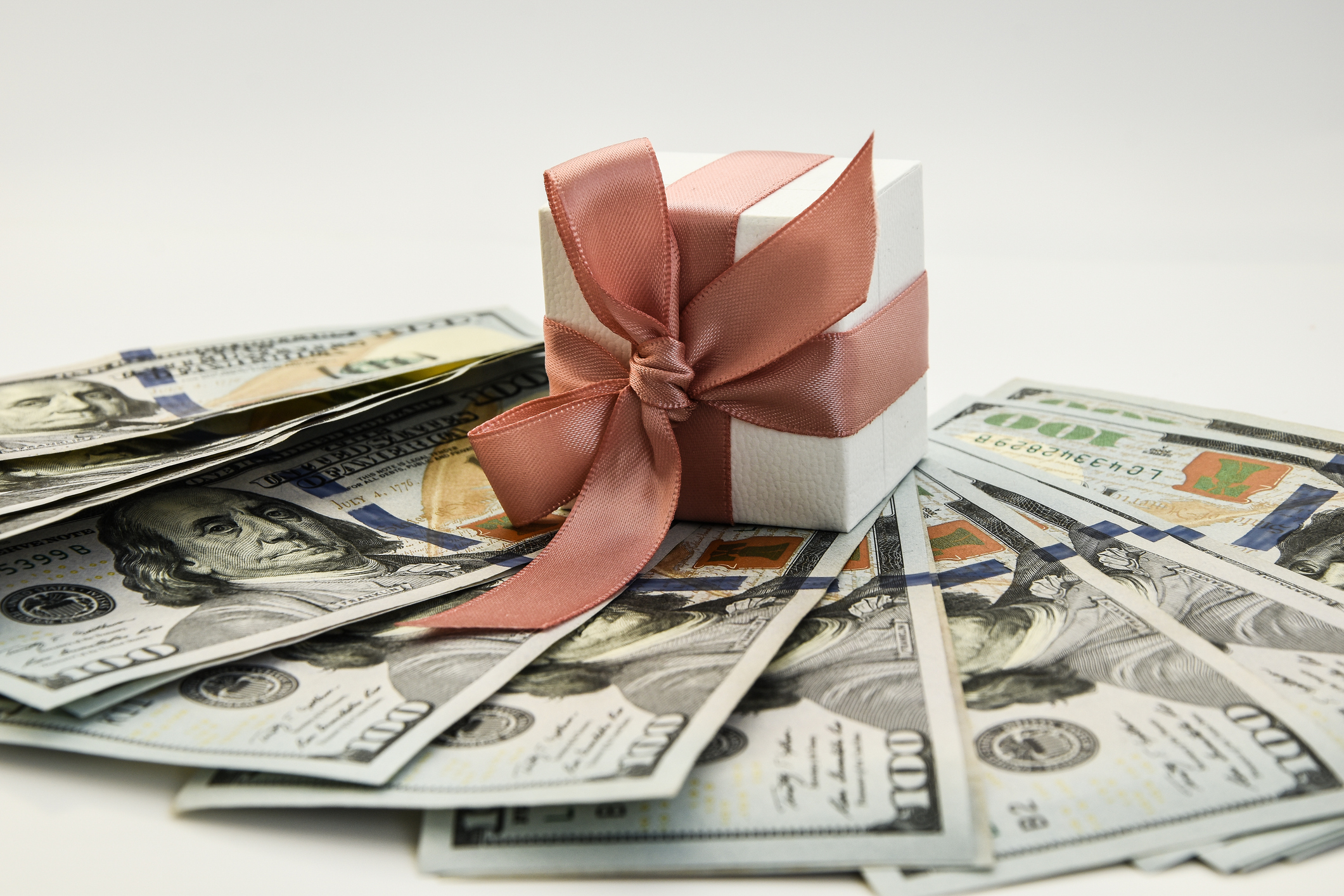 US dollar bills placed underneath a white gift box with a neat bow