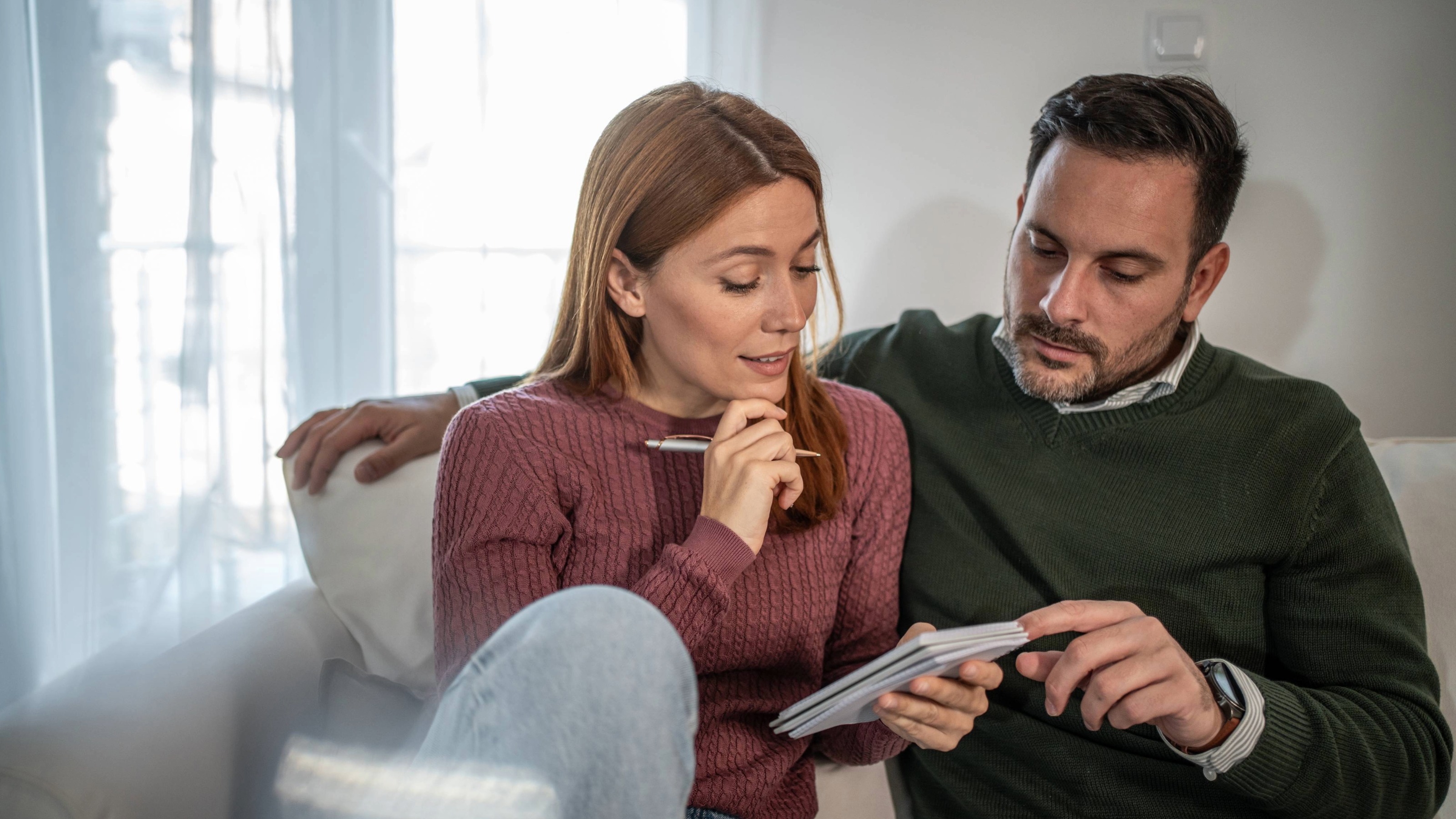 A couple sitting together on a sofa, focused on reviewing financial documents and planning their investments.