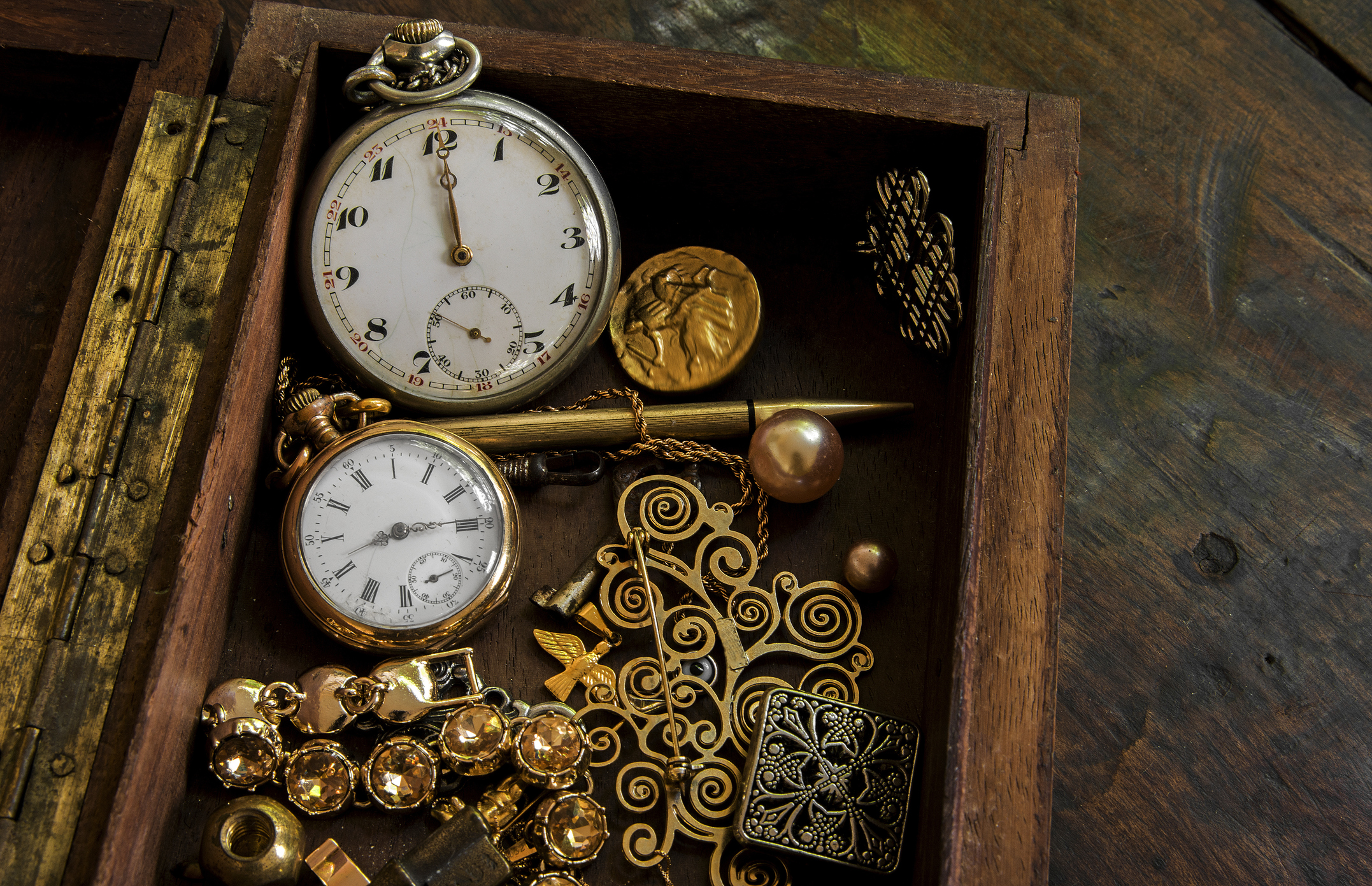 A vintage wooden box filled with gold jewelry and antique pocket watches representing a diverse silver and gold collection.