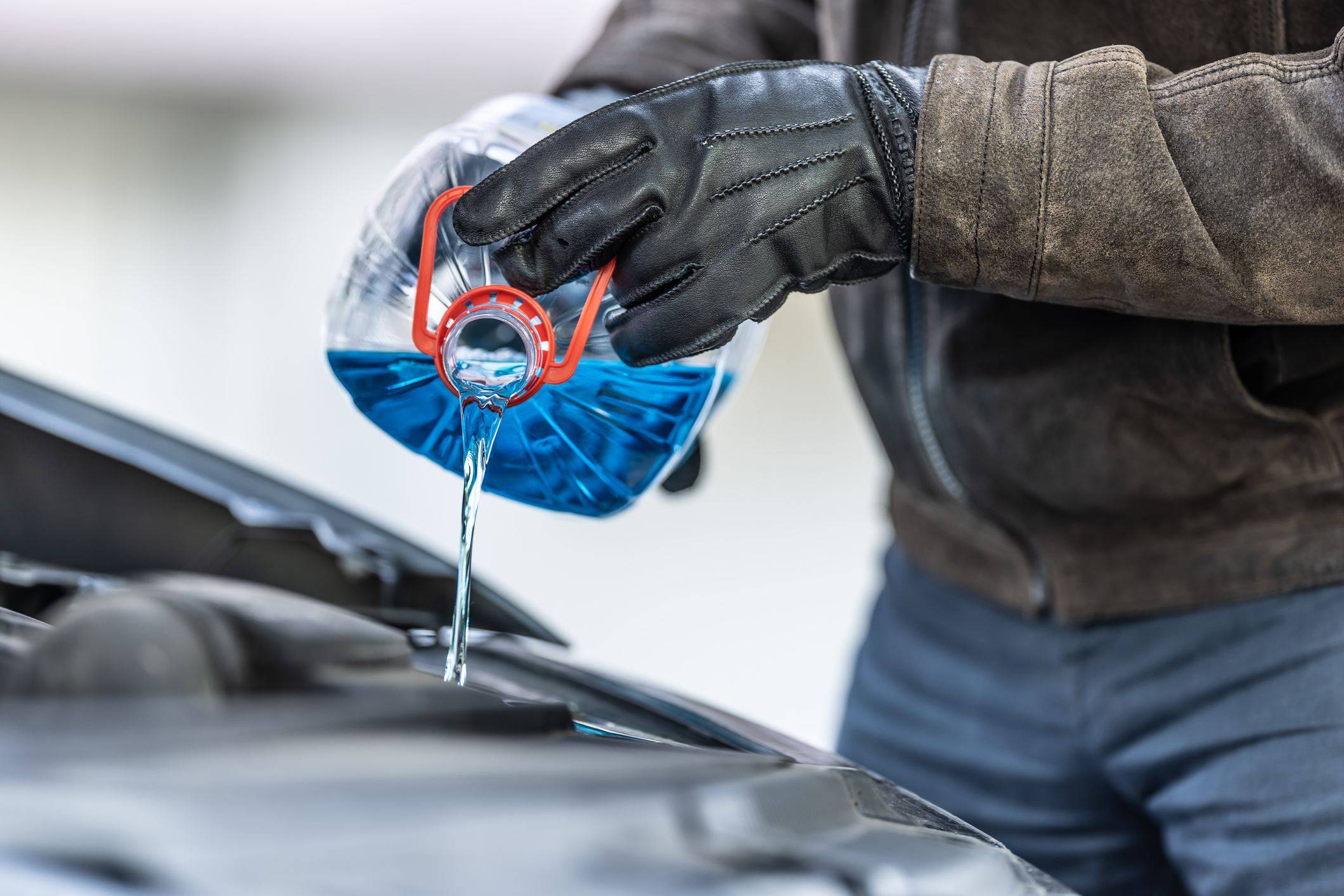 A person carefully pouring antifreeze into a car's engine coolant reservoir.