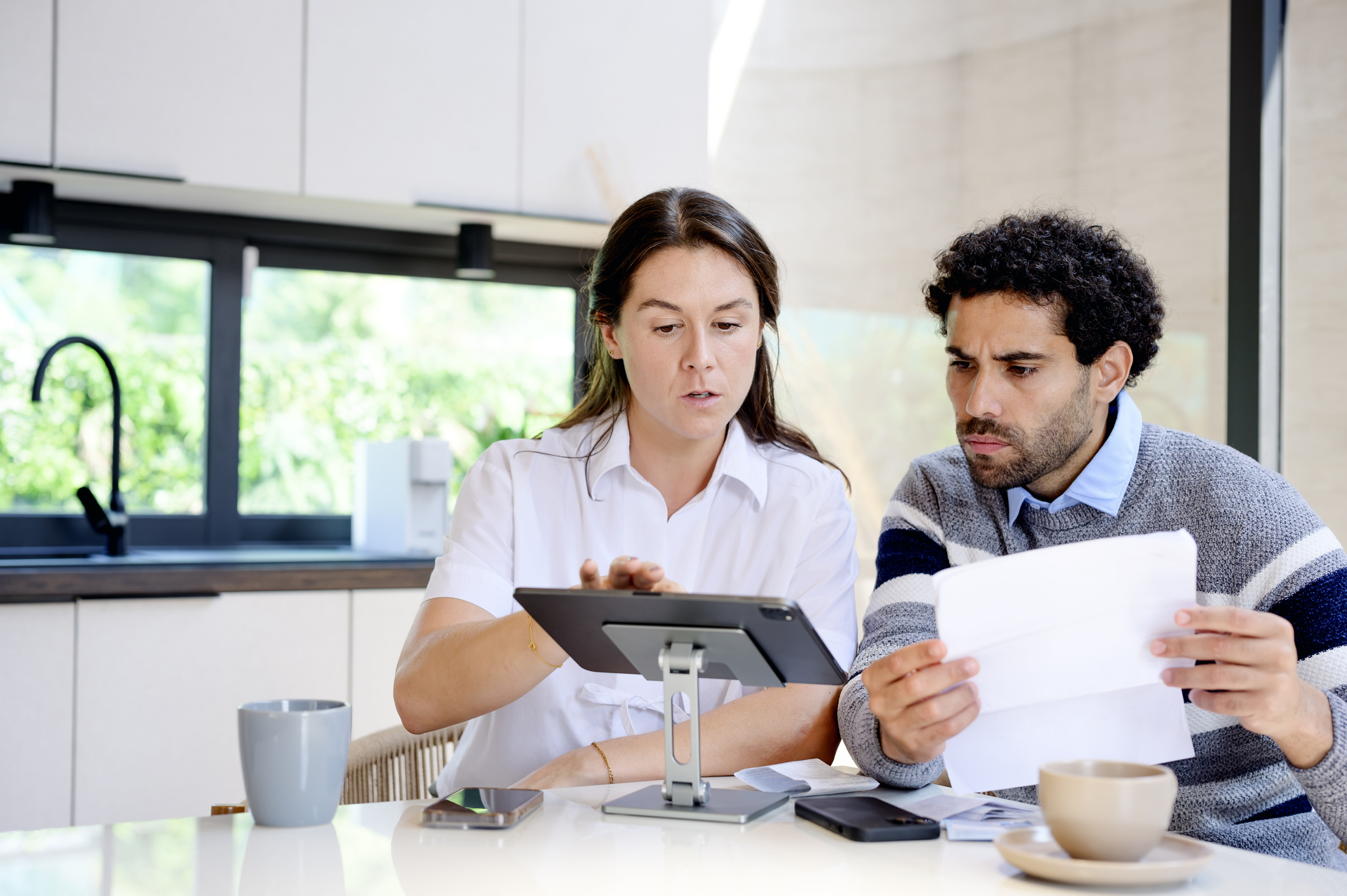 A couple focused on personal finances while reviewing documents and a laptop at a kitchen table.