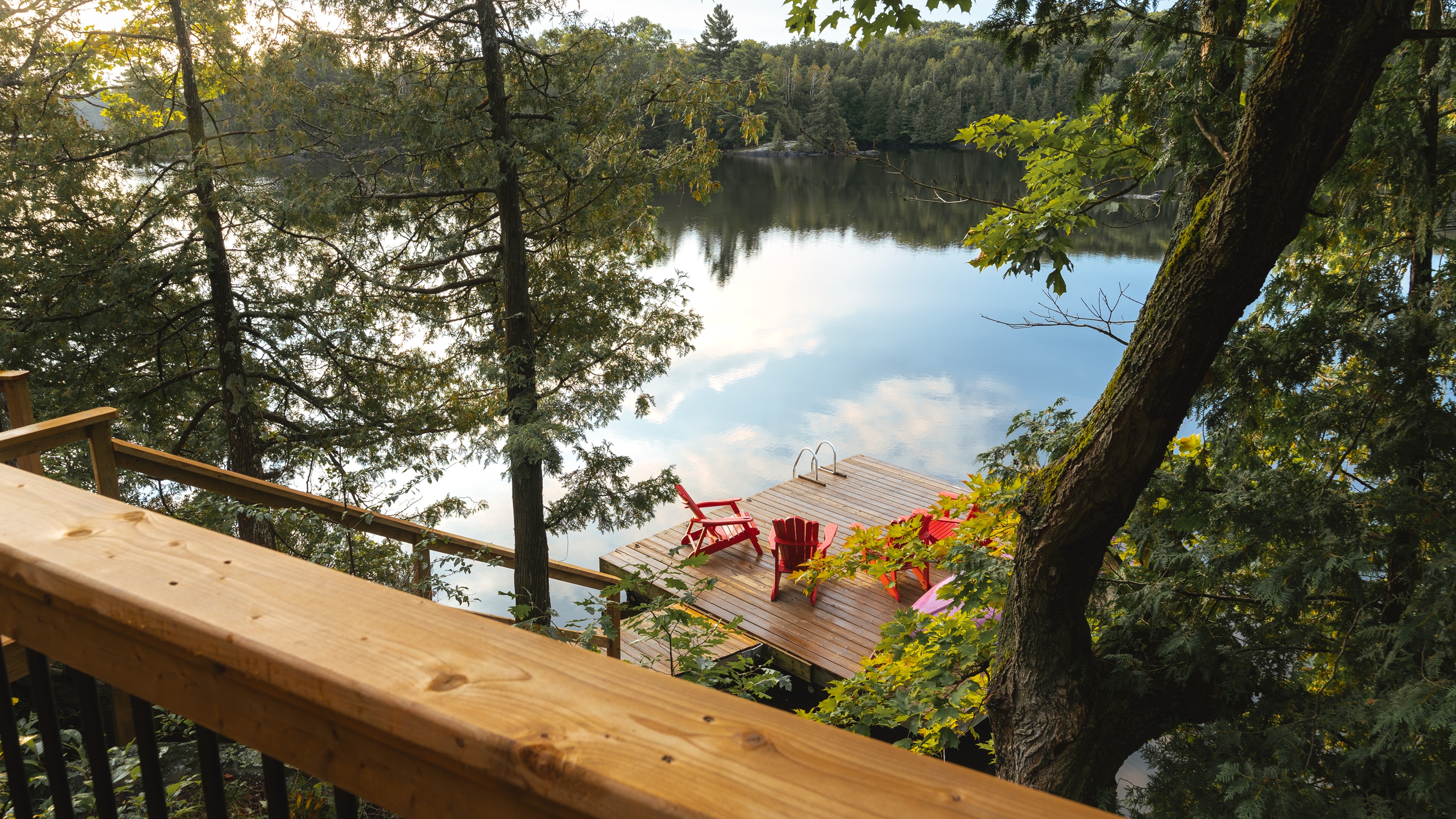 A serene view of a calm lake and a wooden dock seen from a balcony with glass railings.