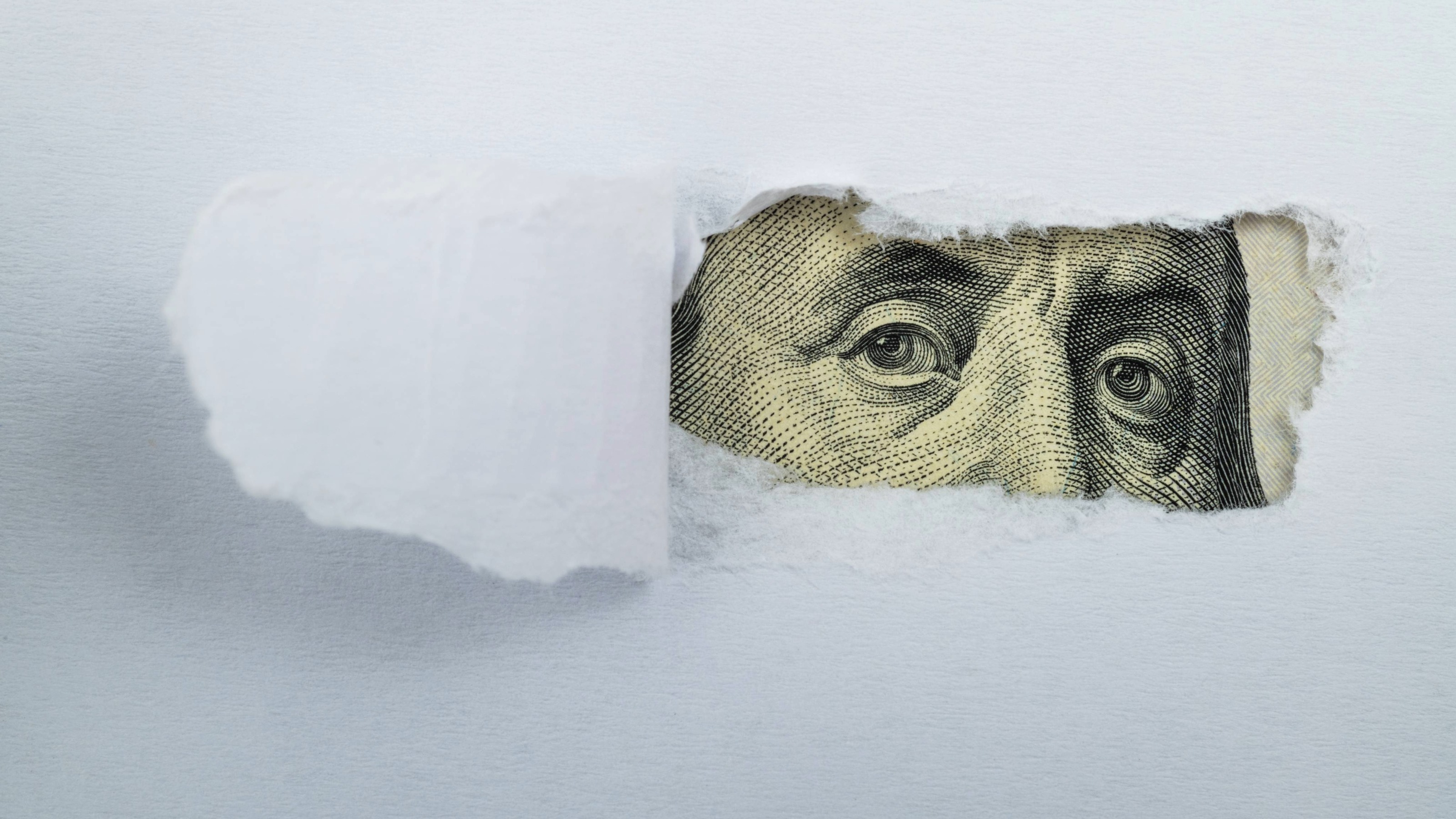 A visual of torn white paper revealing a Benjamin Franklin hundred-dollar bill underneath.