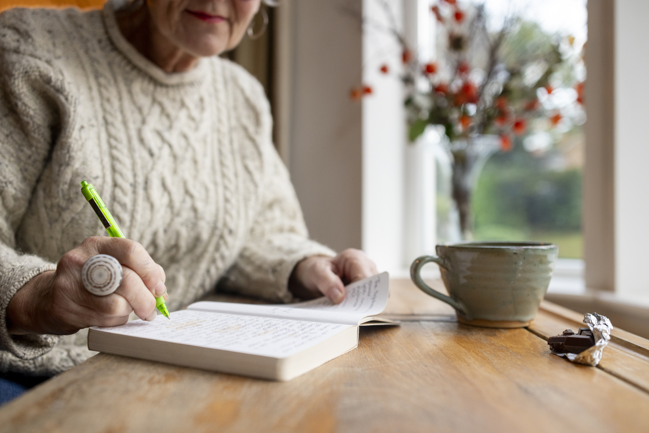 A woman sitting at a desk carefully writing in a journal to track her emotional spending triggers.