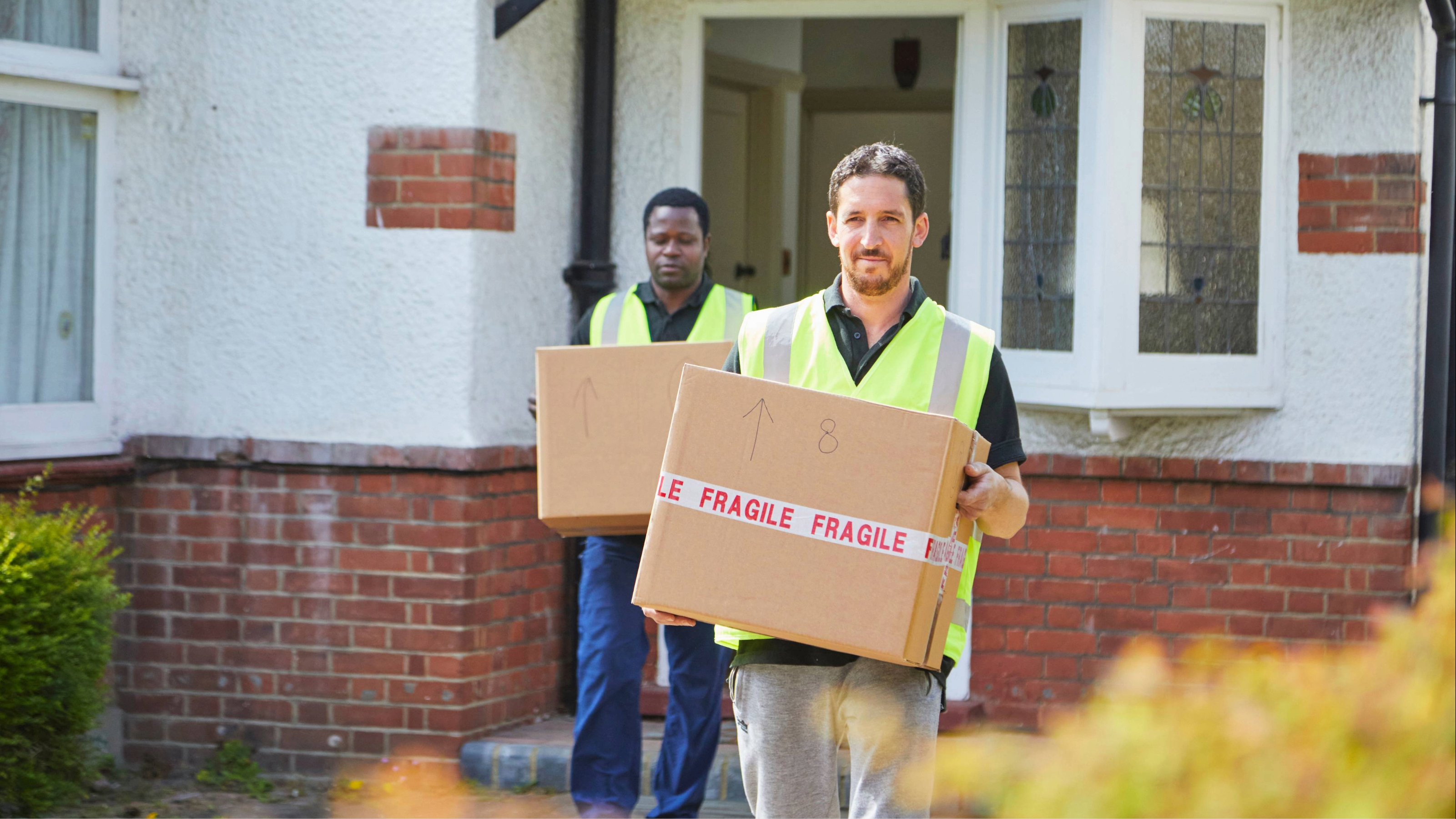 Two professional movers in uniform carrying boxes during a household move.