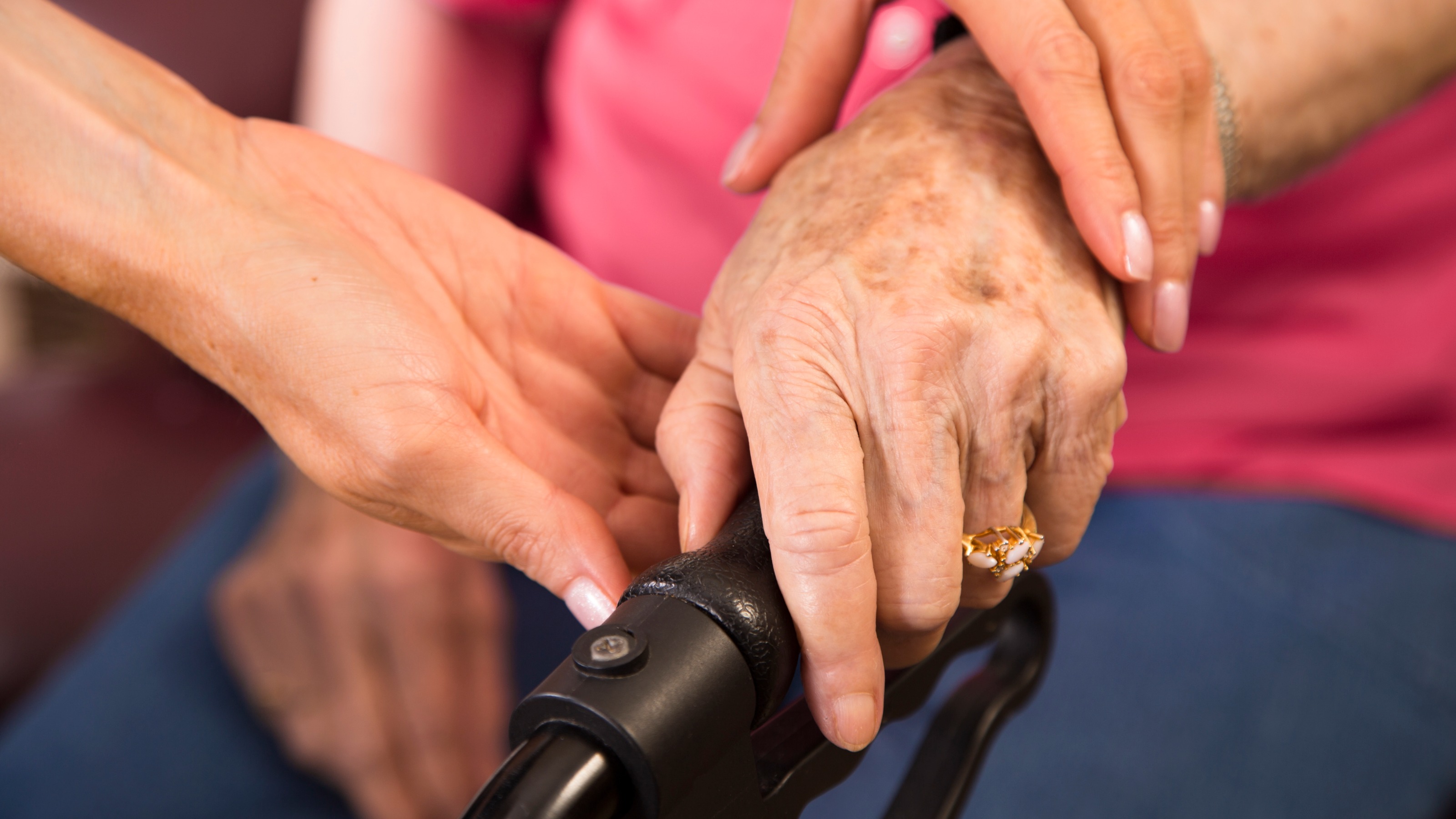 Close-up of a caregiver's hands supporting a senior citizen using a walker, emphasizing the support needed in late-life stages.