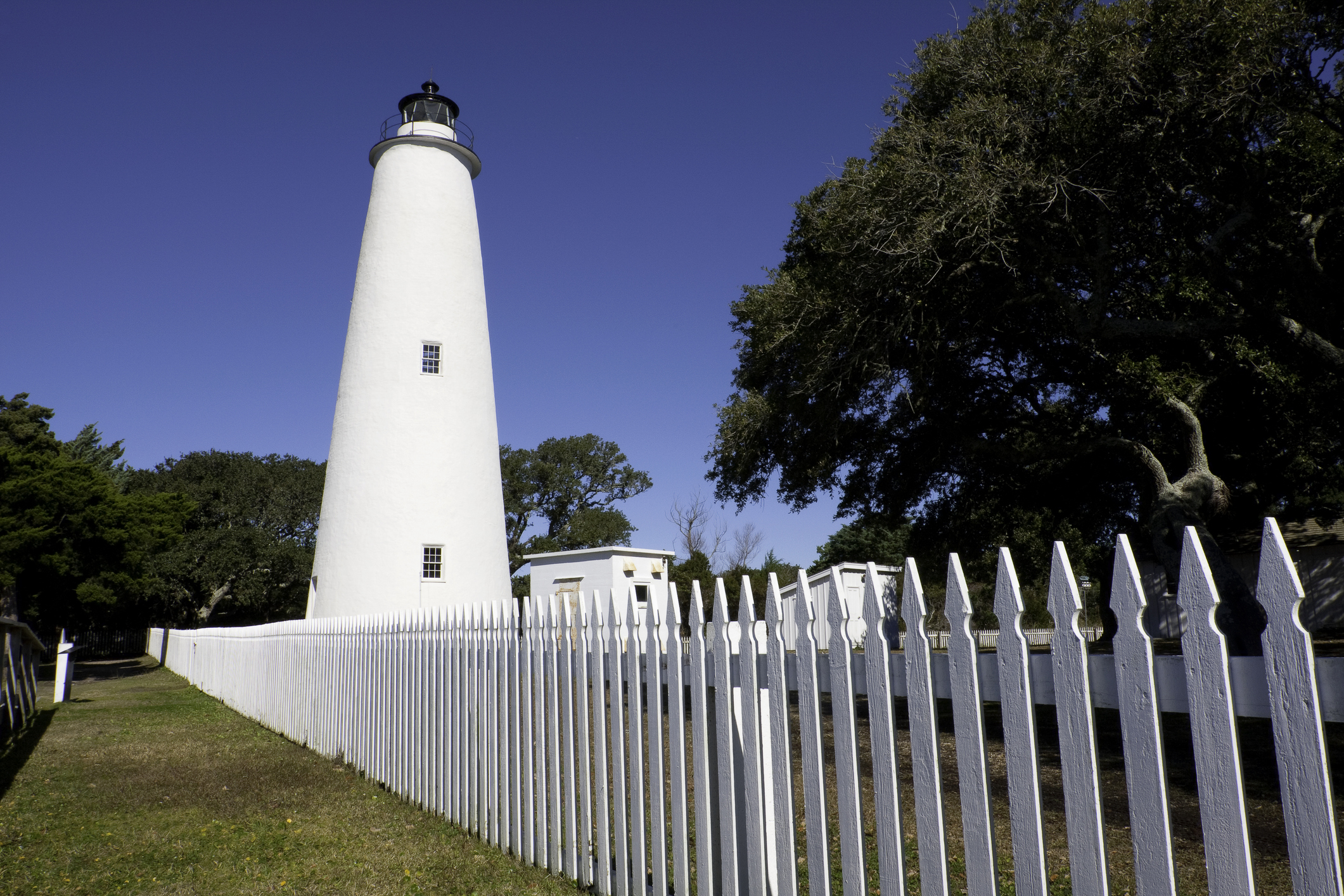 The white Ocracoke Island Lighthouse standing behind a white picket fence on the Outer Banks.