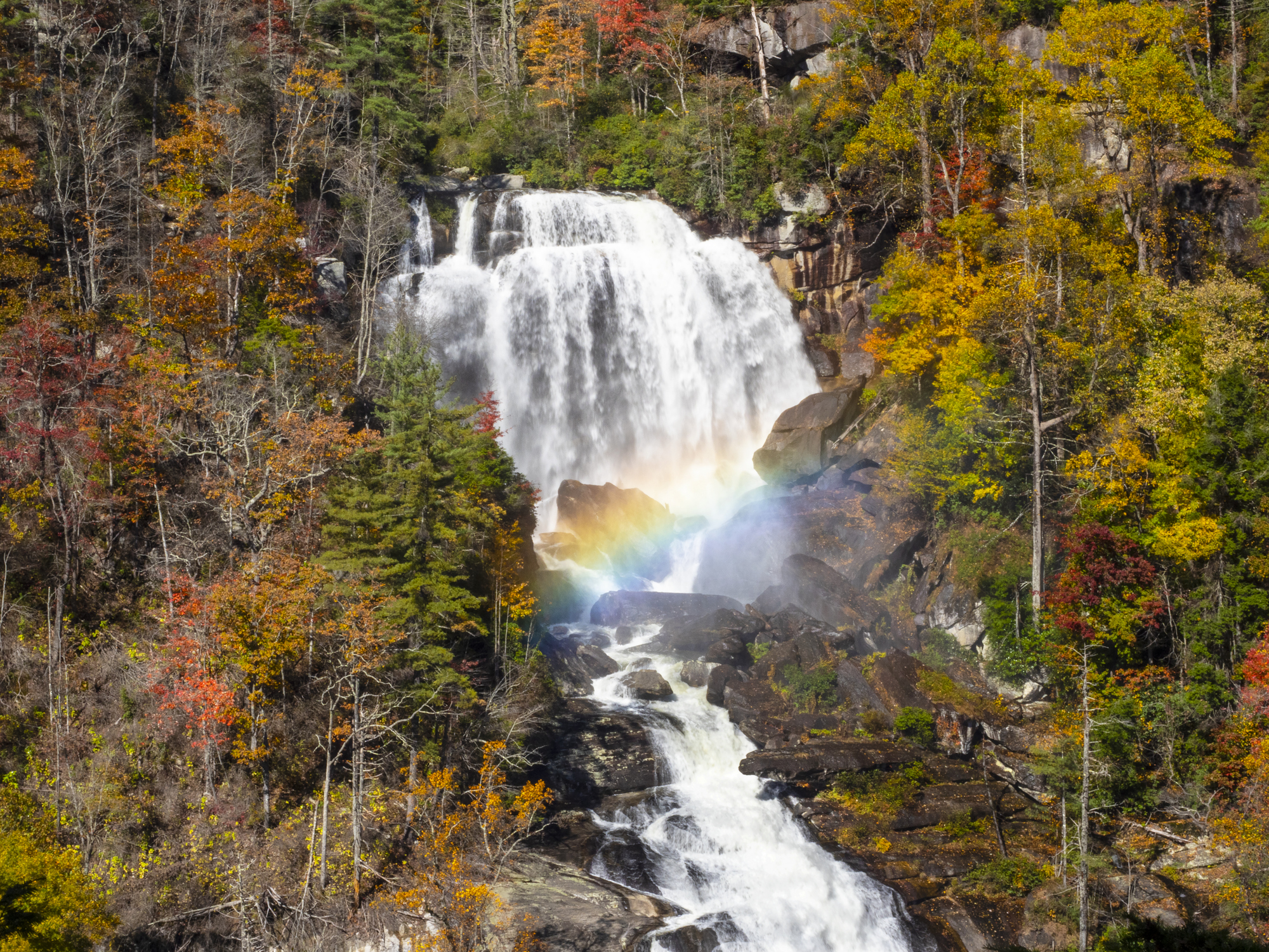 A powerful waterfall at Whitewater Falls with a rainbow visible in the mist over the rocks.